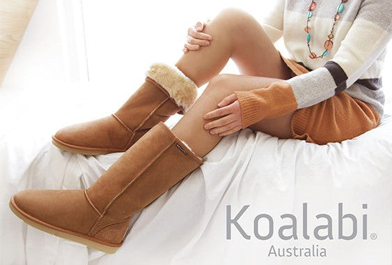 A woman sits on a bed, casually dressed, showcasing her stylish winter boots - Koalabi Australia